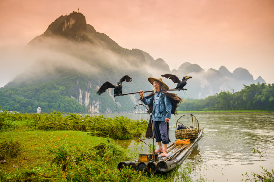 Hombre paseando en canoa en yangshuo cormoran China